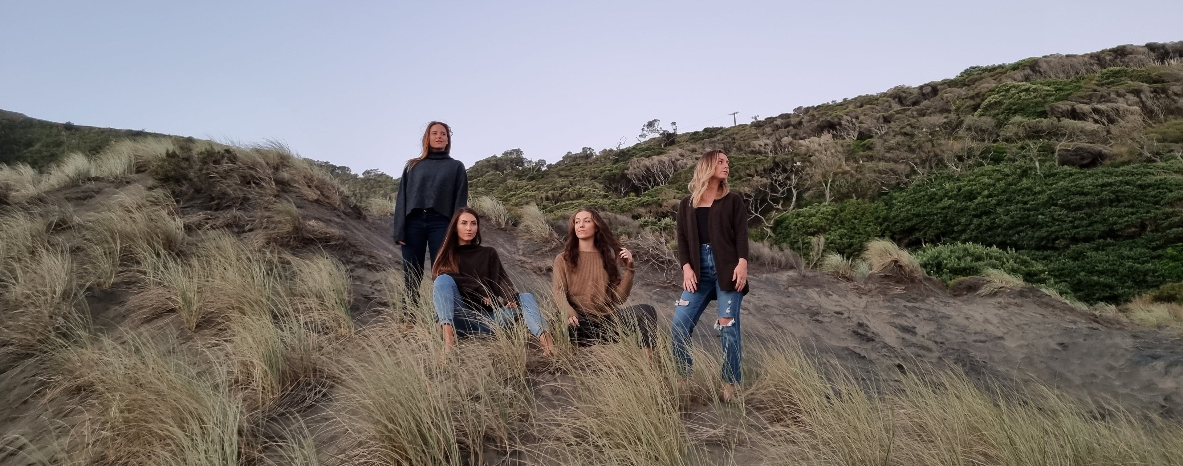 Four people standing on a grassy hillside with a clear sky.