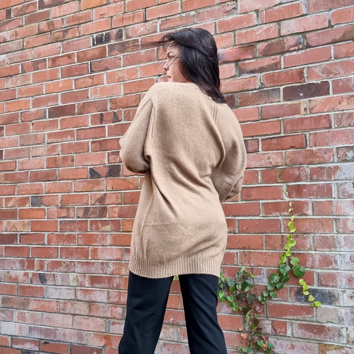 Unisex Mens Jumper. Black haired woman wearing oversize jumper in a caramel brown colour. Sweater made from Merino Possum Angora and Silk. Knitted locally in New Zealand by an Ethical, sustainable female designer. Jumper has a thin rolled crew neck detail and long sleeves and small tripe detail on the centre back neckline