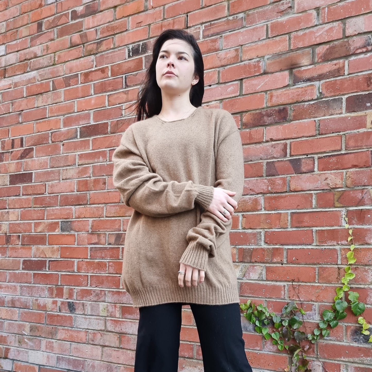Unisex Mens Jumper. Black haired woman wearing oversize jumper in a caramel brown colour. Sweater made from Merino Possum Angora and Silk. Knitted locally in New Zealand by an Ethical, sustainable female designer. Jumper has a thin rolled crew neck detail and long sleeves