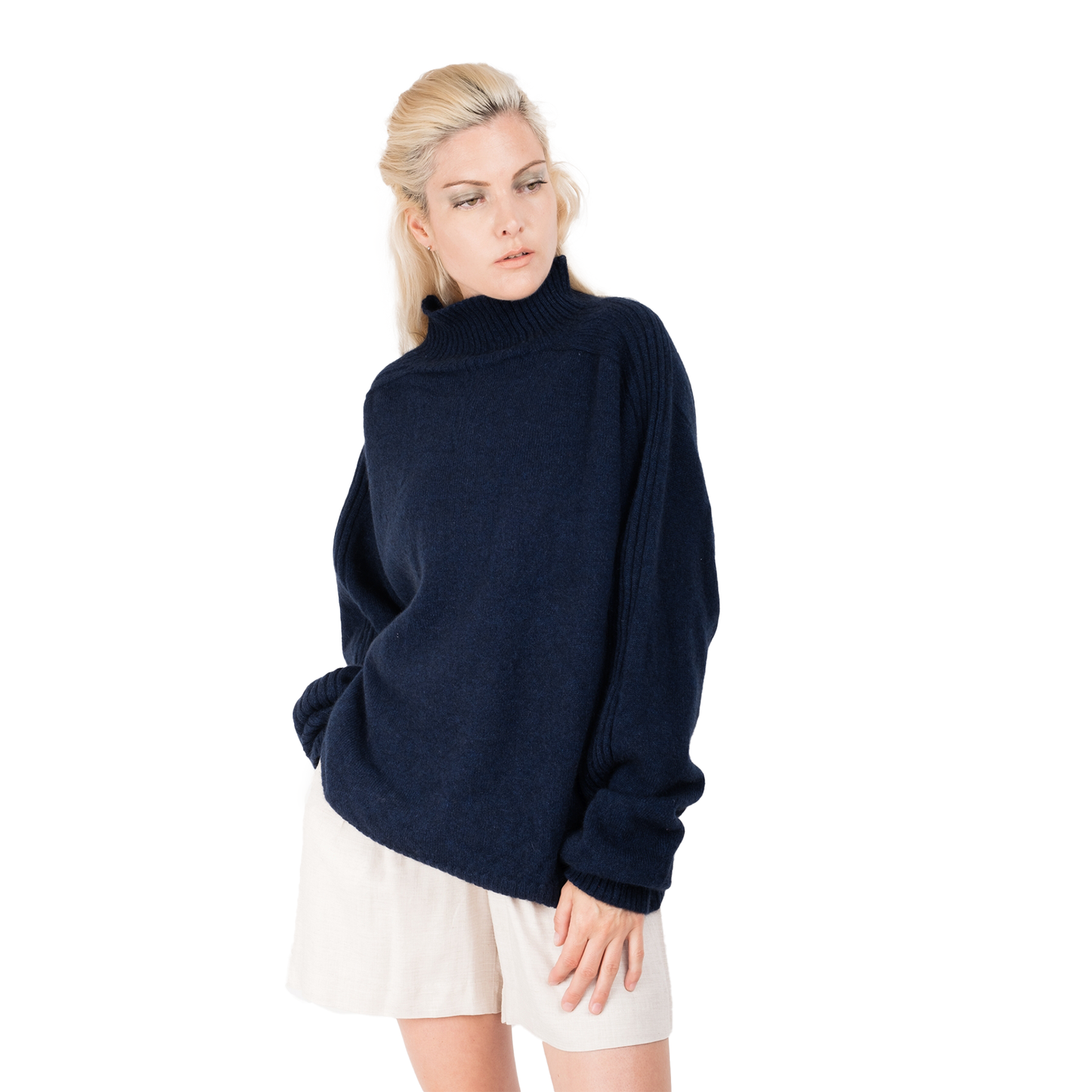 Blond lady wearing a deep inky blue knitted jumper. Full oversizebody with a  ribbed hem. Turtleneck and ribbed cuffs. Sweater made from Merino possum and nylon and made in new zealand. She is facing the front with her arm relaxed down by her side showing off the ribbed line detail on the top of the sleeves of the sweater