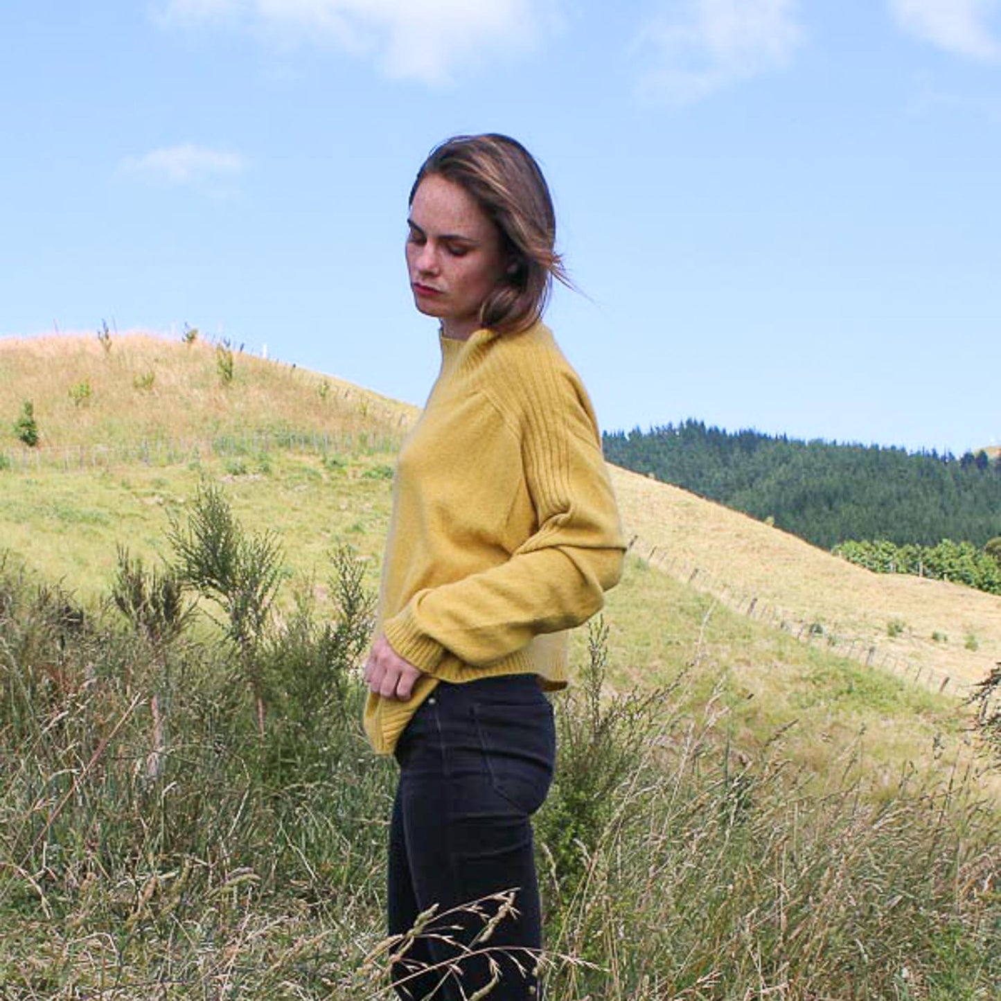 Sports stripe sweater with a turtle neck and long sleeves in a sunshin yellow. Made in NZ from New Zelaand Merino Possum and Silk. Girl in a field showing side of the jumper