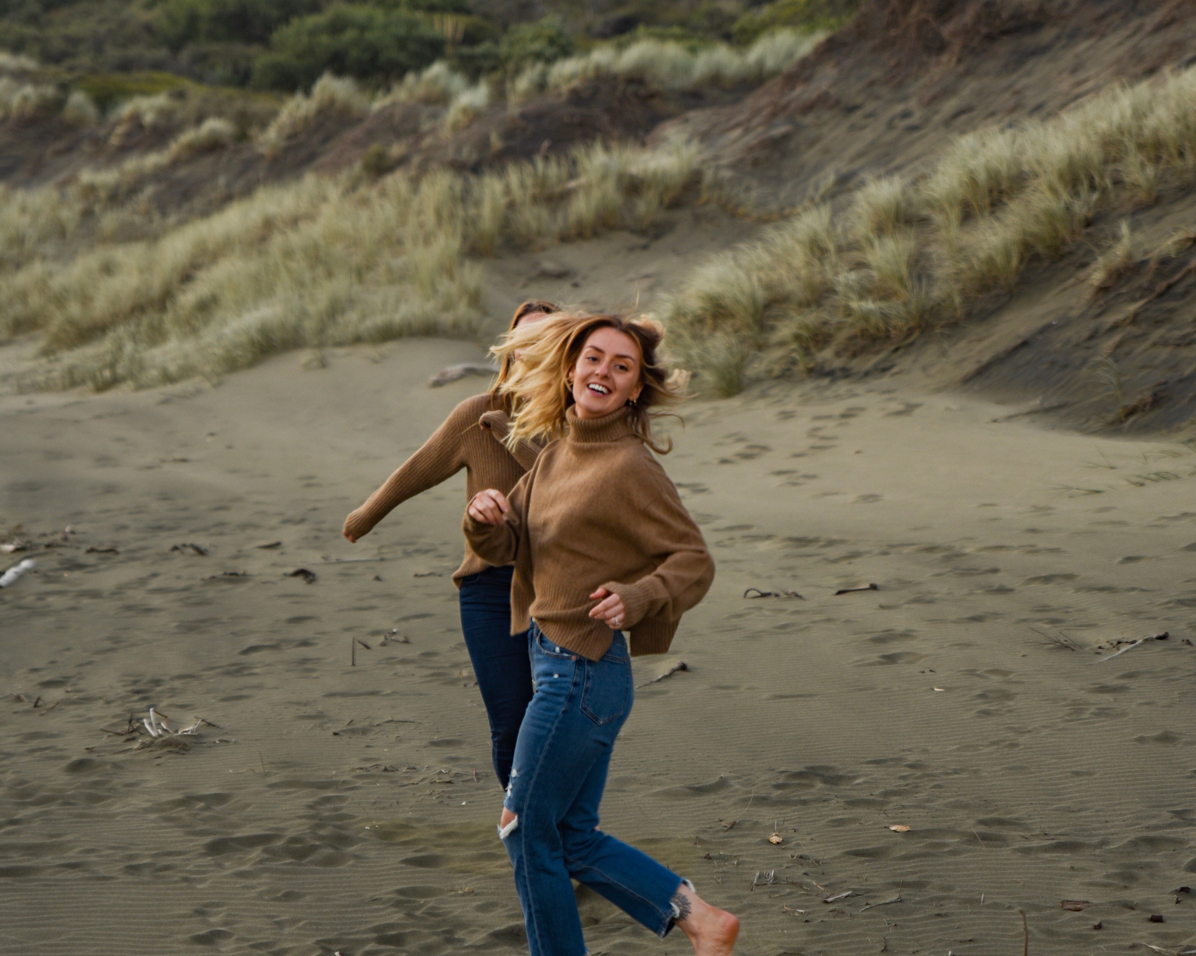 Two people running on a beach with a dog