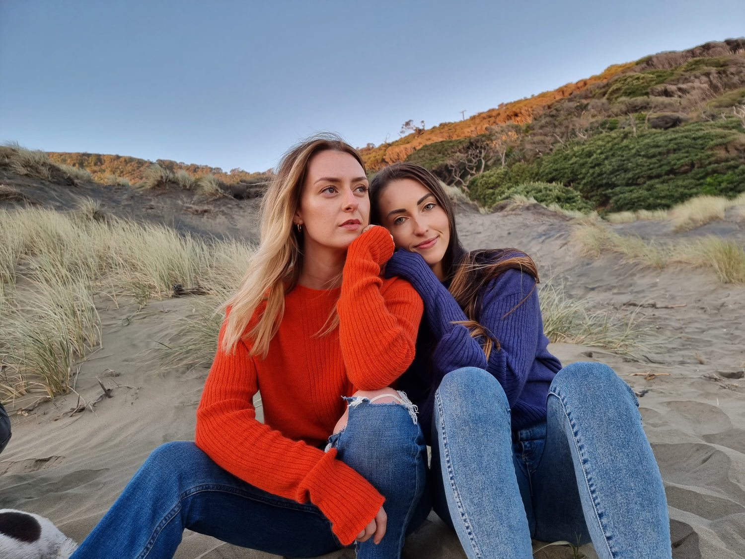 2 women sitting on the beach wearing bright cosy knitwear