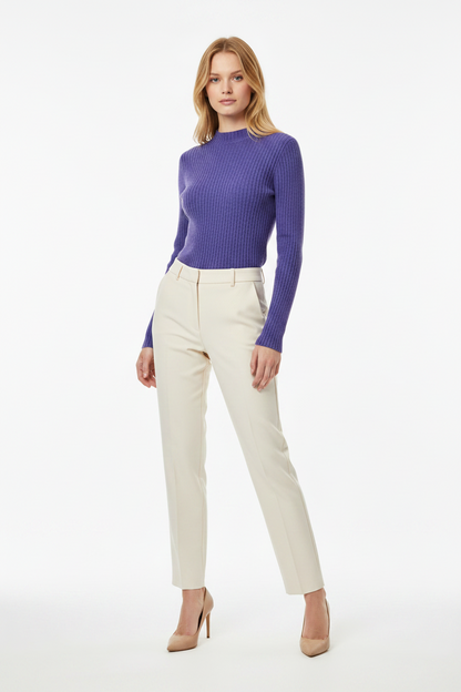 Woman wearing a purple ribbed sweater and beige pants on a white background