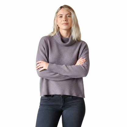 Woman wearing a smoke gray turtleneck sweater and dark jeans on a white background