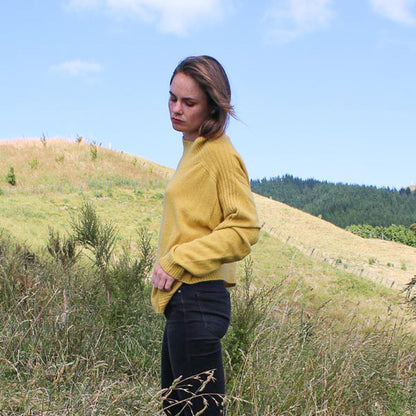 Sports stripe sweater with a turtle neck and long sleeves in a sunshin yellow. Made in NZ from New Zelaand Merino Possum and Silk. Girl in a field showing side of the jumper